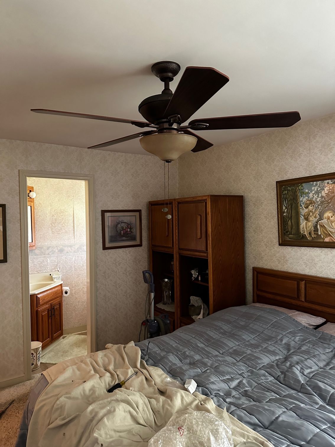 Bedroom with unmade bed, ceiling fan, wooden dresser, and open bathroom door