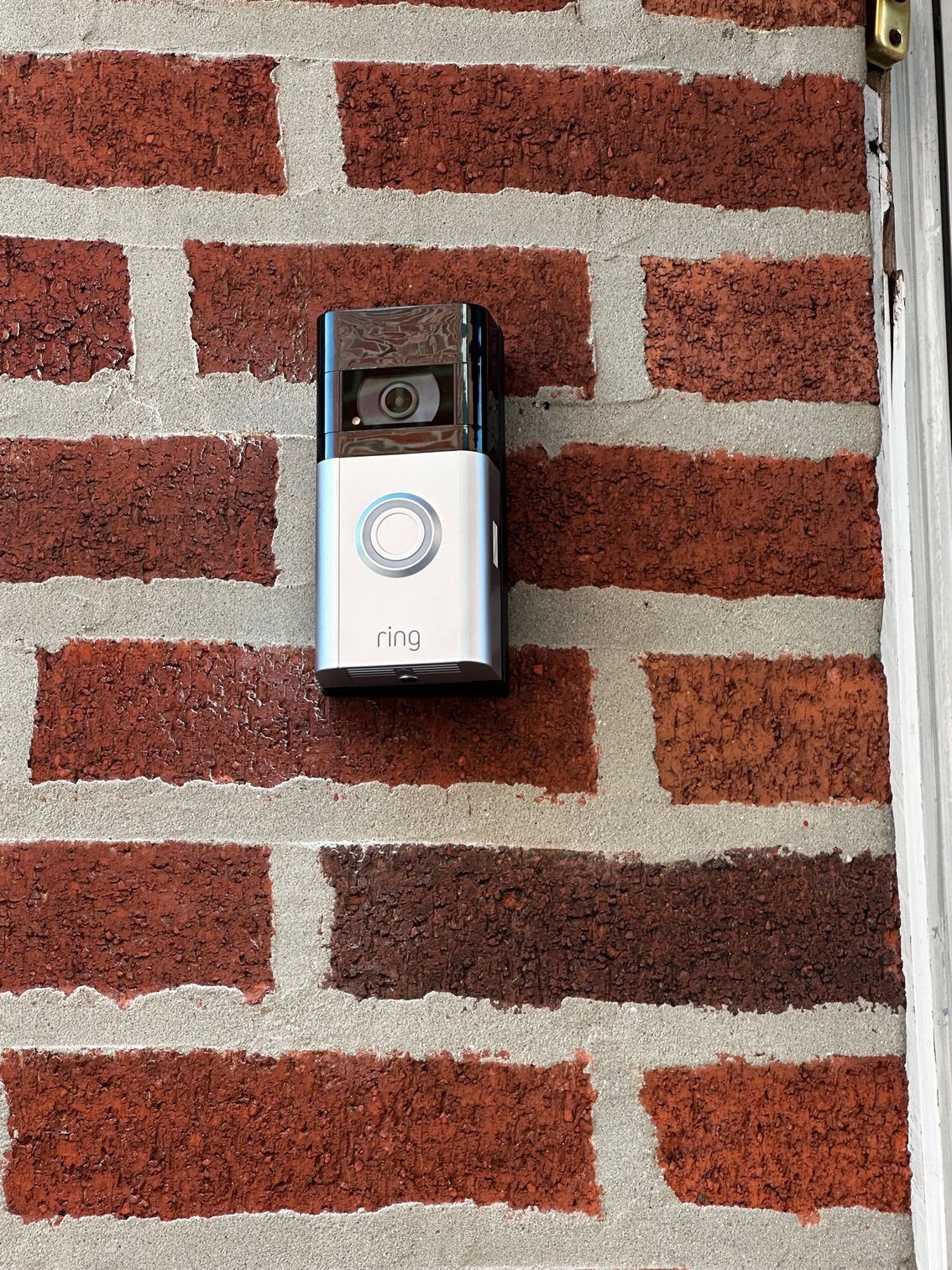 Doorbell camera mounted on a brick wall, with a silver and black faceplate.