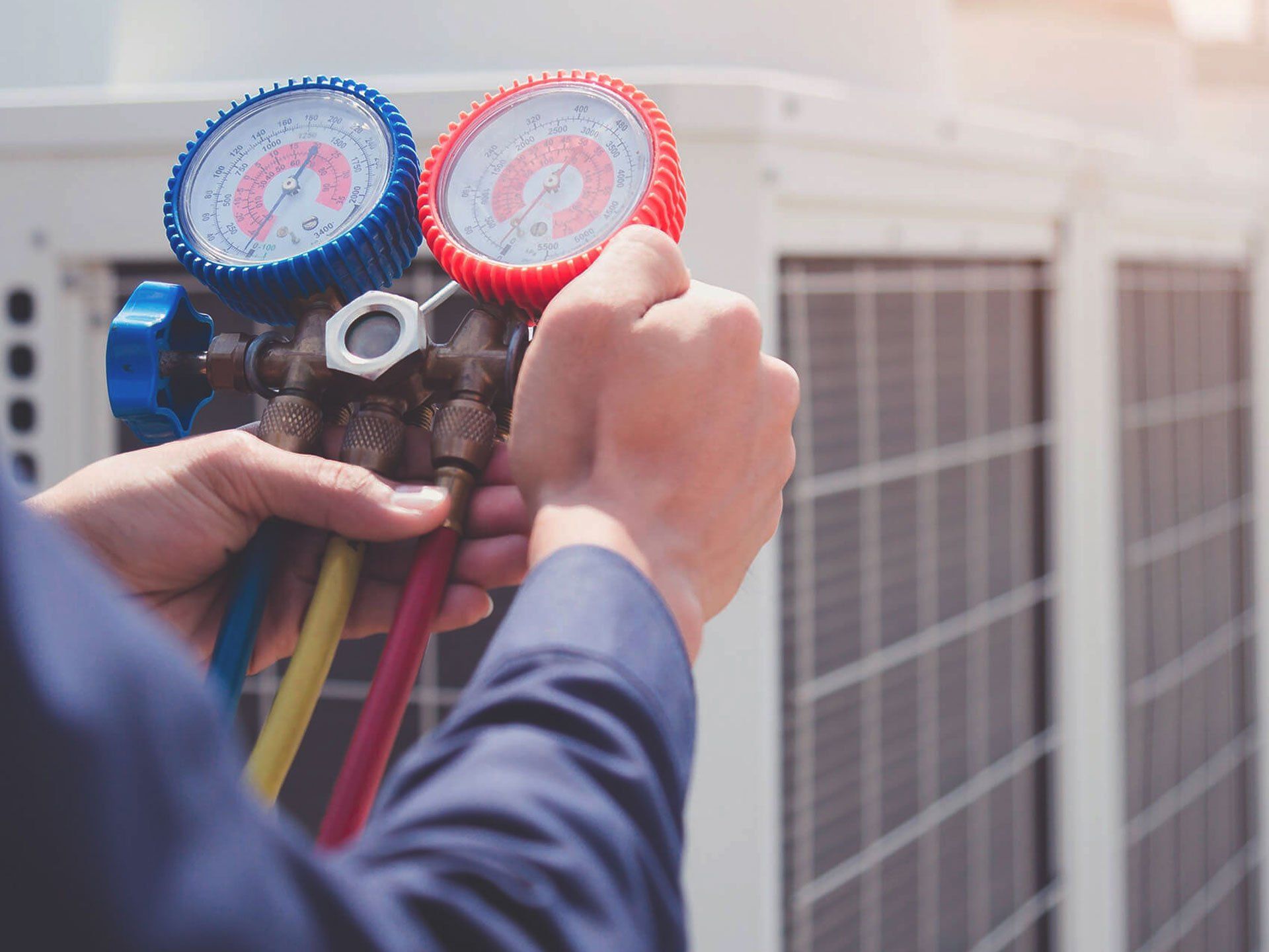 Technician adjusting gauges on an outdoor air conditioning unit with hoses attached