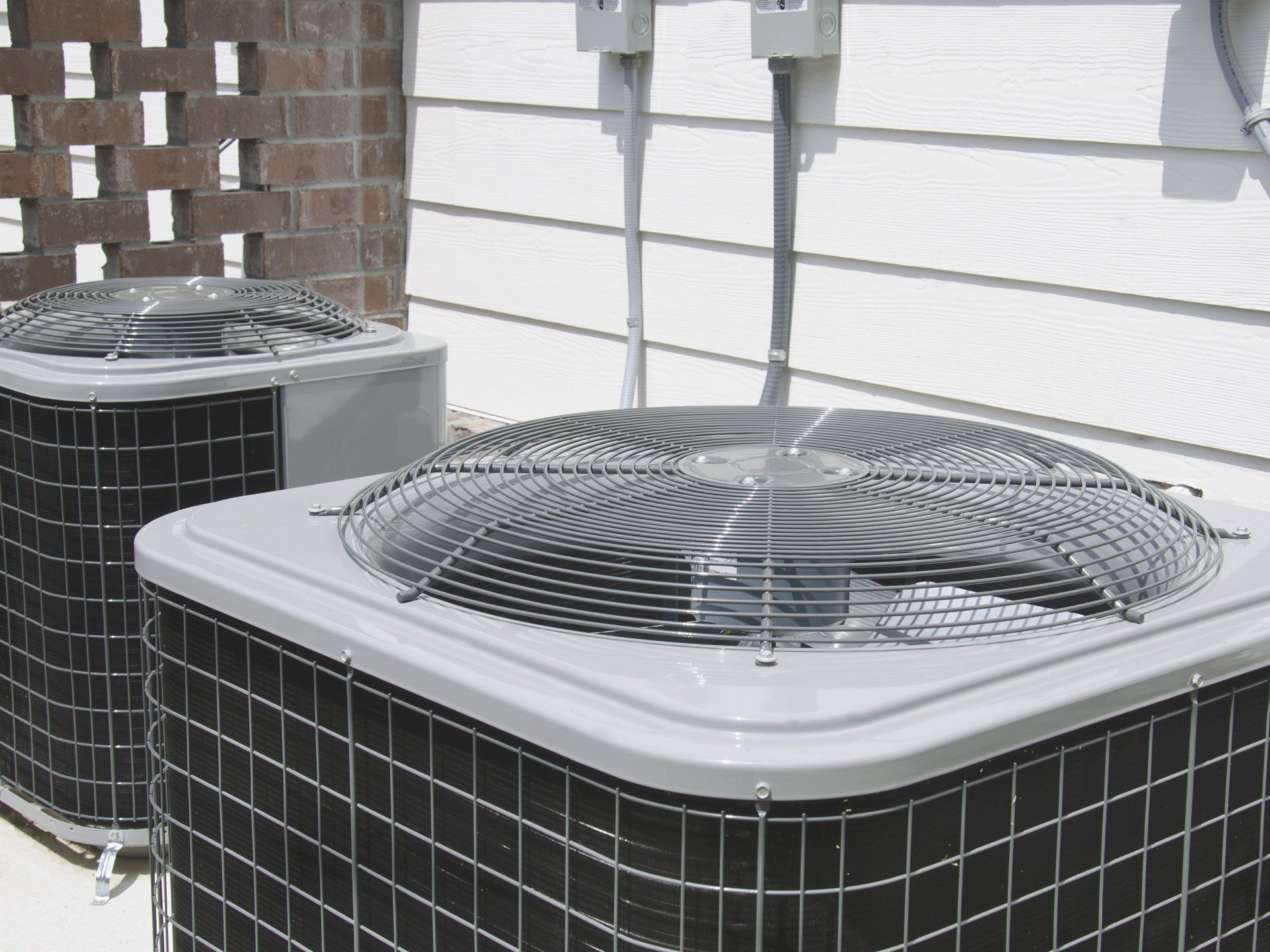 Two outdoor air conditioning units beside a white house wall