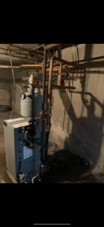 Basement boiler and water heater with exposed copper pipes and valves against a concrete wall