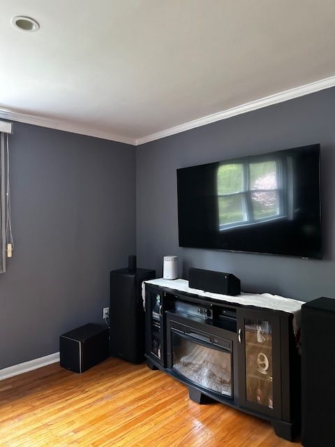 Modern living room corner with gray walls, hardwood floor, wall-mounted TV, and black fireplace console