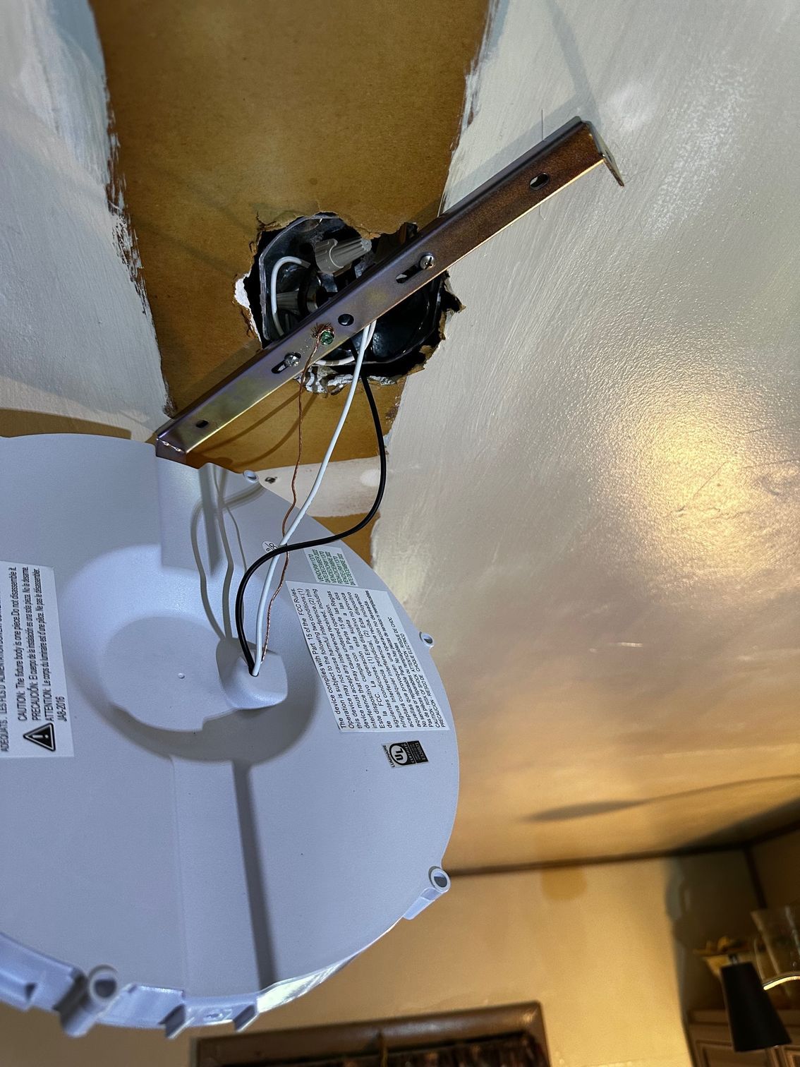 Ceiling-mounted smoke detector with exposed wiring and a detached white cover hanging below