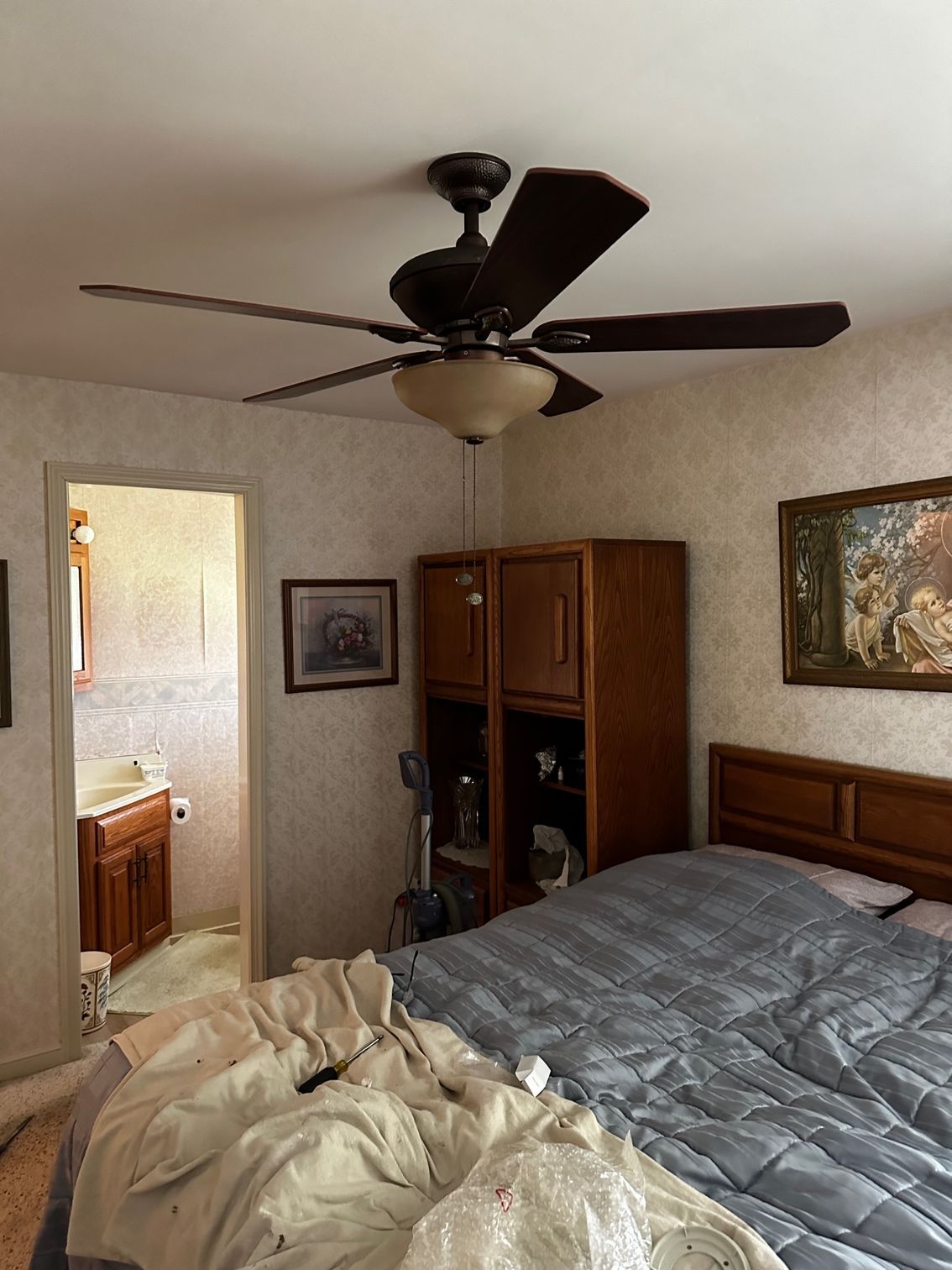Bedroom with unmade bed, ceiling fan, wooden dresser, and bathroom doorway visible.