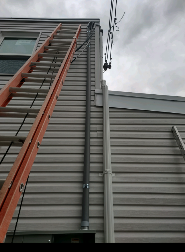 Ladder leaning against a gray metal building under cloudy sky, viewed from below