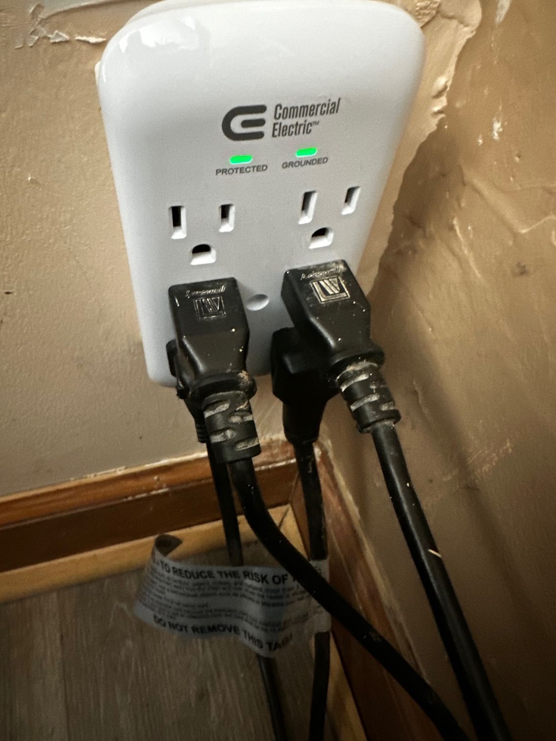 Two black plugs in a white wall outlet adapter with indicator lights on a brown wall.