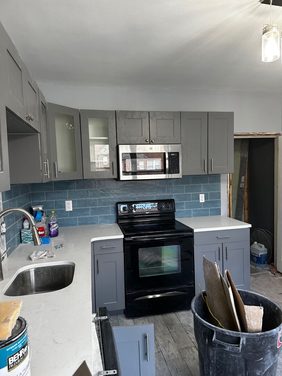 Gray kitchen with blue backsplash, black stove, and cabinets under renovation, with tools on the counter