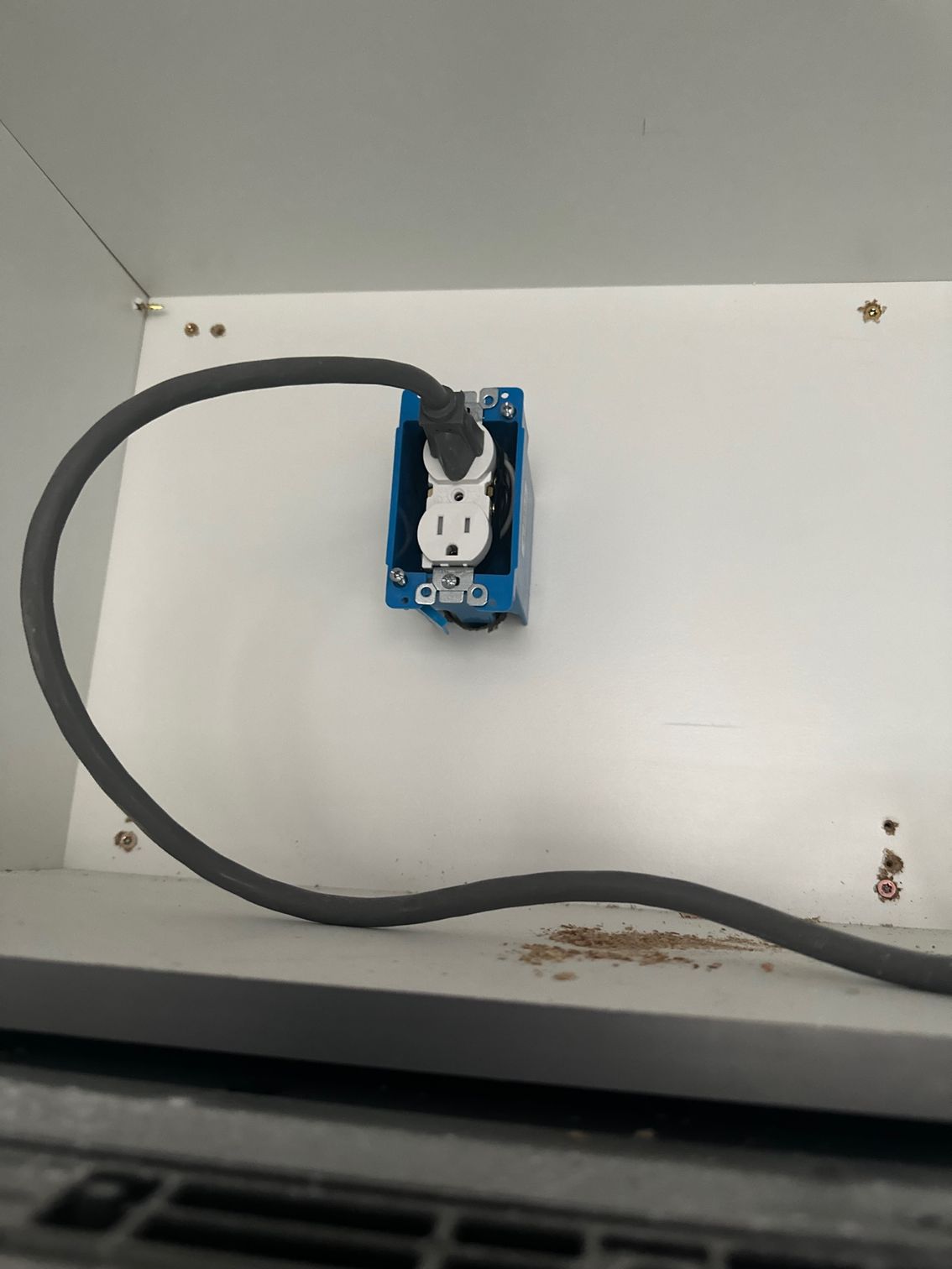 White wall outlet with a black cord plugged in and running across the wall near the floor.
