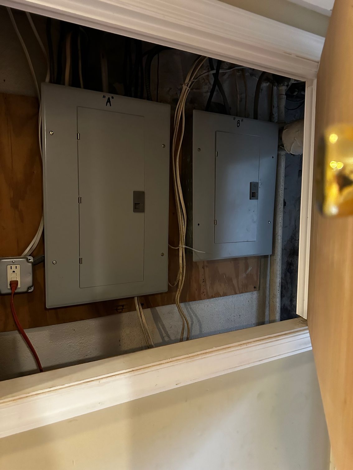 Open wall panel with two gray electrical breaker boxes and exposed wiring.