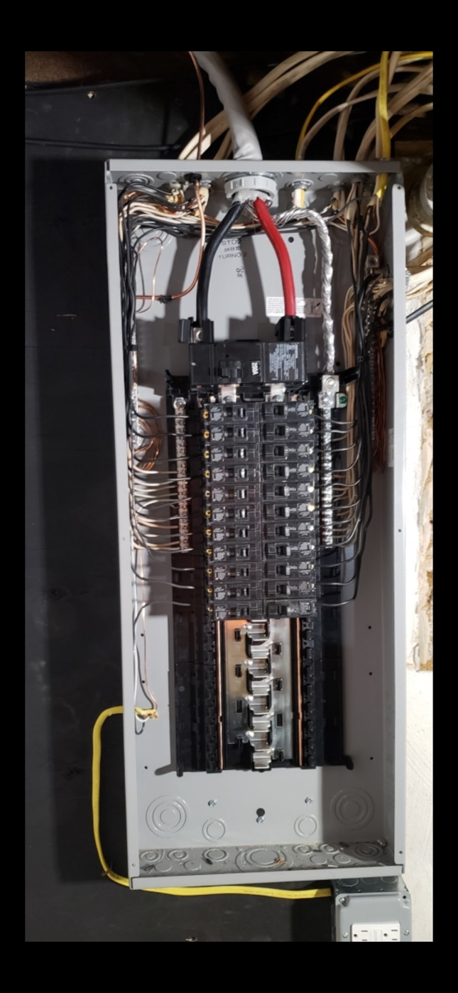 Electrical breaker panel with rows of black circuit breakers and bundled wires inside a metal cabinet
