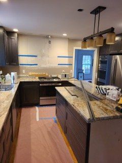 Modern kitchen with granite island, dark cabinets, stainless appliances, and blue painter’s tape on the walls