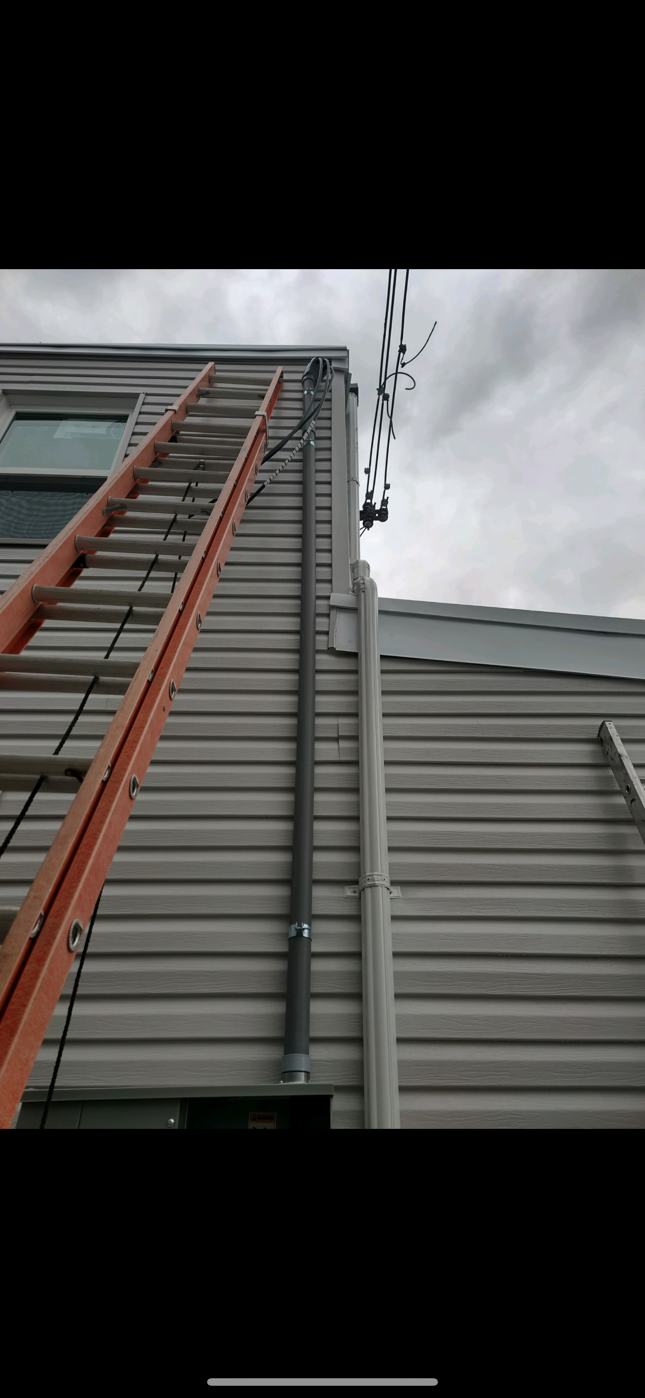 Red ladder leaning against a gray house wall under a cloudy sky.