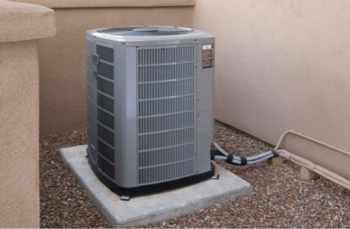 Outdoor air conditioner unit on a concrete pad beside a house wall and gravel yard