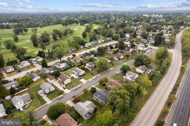 Aerial view of a suburban neighborhood beside a road, with houses, trees, and golf course greens nearby