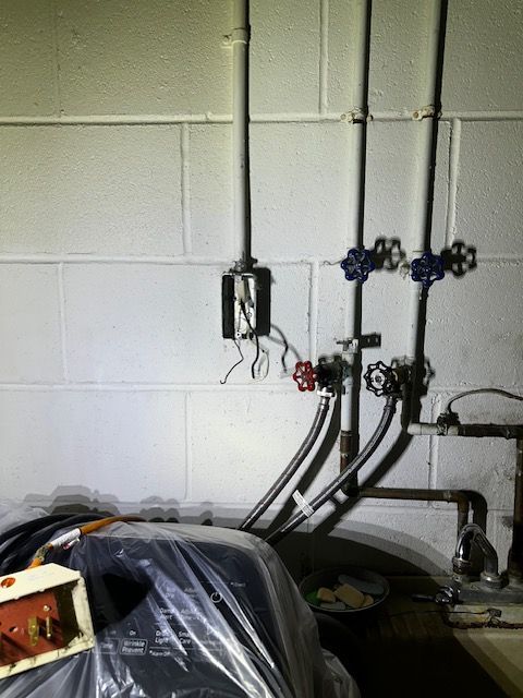 Utility pipes and valves on a cinderblock wall above a covered machine in a basement utility area
