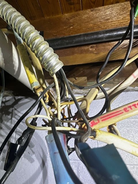 Cluster of tangled black and yellow cables and hoses under wooden boards in a cramped space.