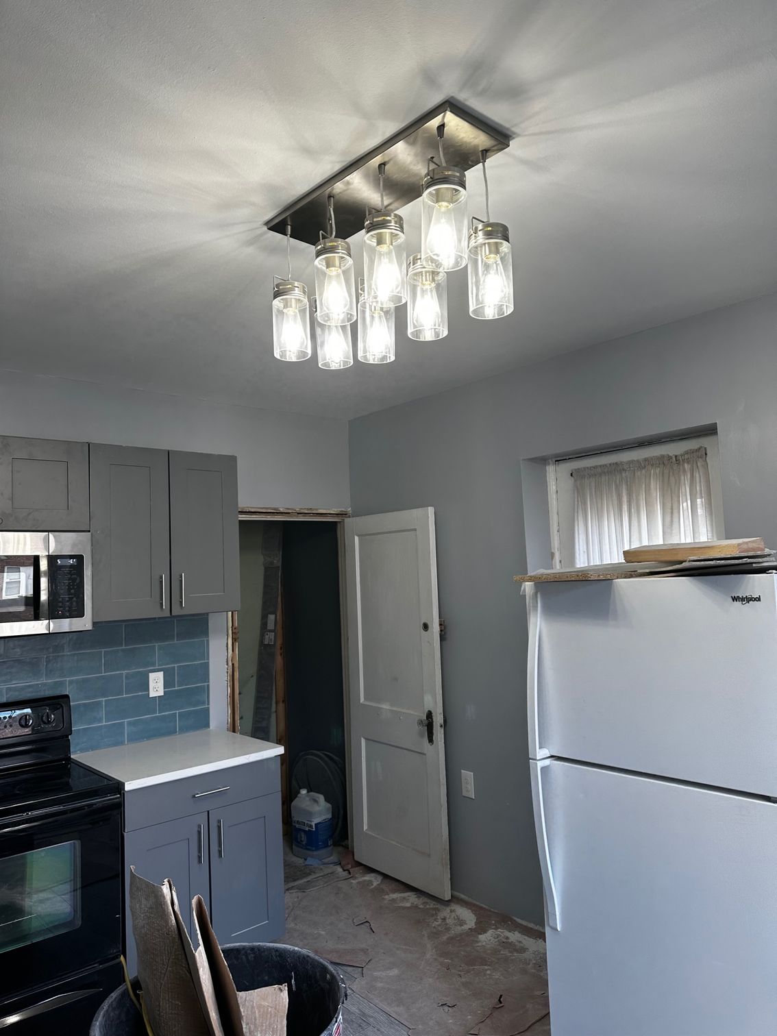 Small kitchen with gray cabinets, white fridge, black stove, and a modern ceiling light fixture.