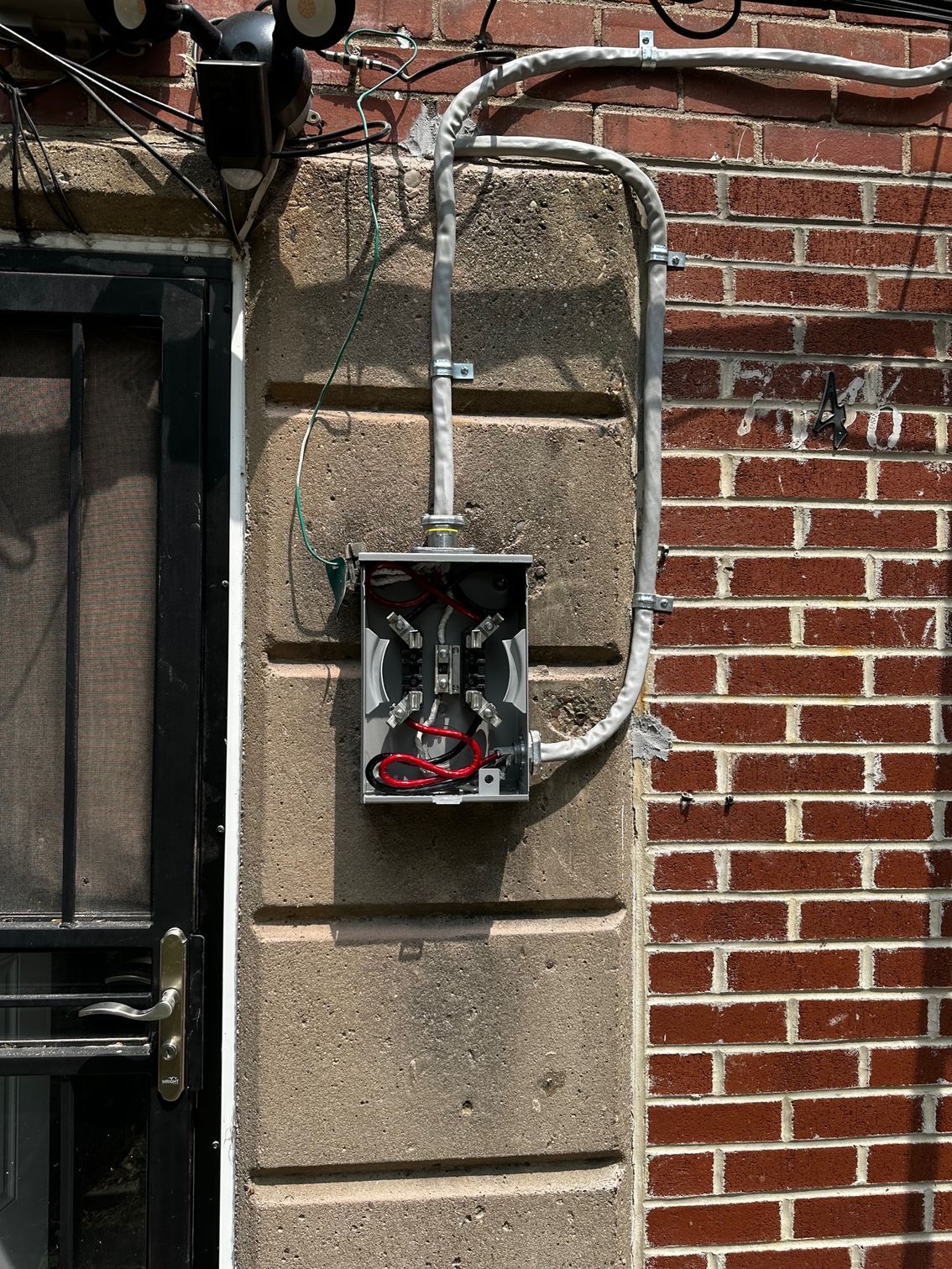 Open electrical meter box mounted on a brick wall with exposed wiring and red components