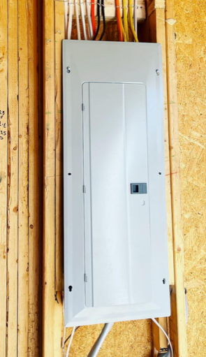 White electrical breaker panel mounted on unfinished wooden wall framing