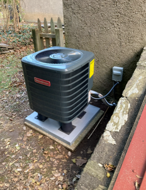 Outdoor HVAC condenser unit on a concrete pad beside a house wall and utility box.