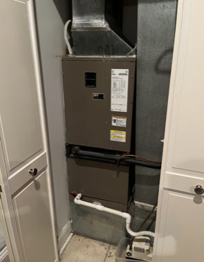 Indoor HVAC unit in a closet with exposed ducts and white pipes.