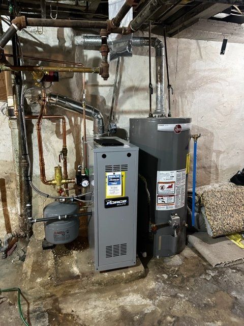 Utility room with furnace, water heater, and exposed pipes against a concrete wall.