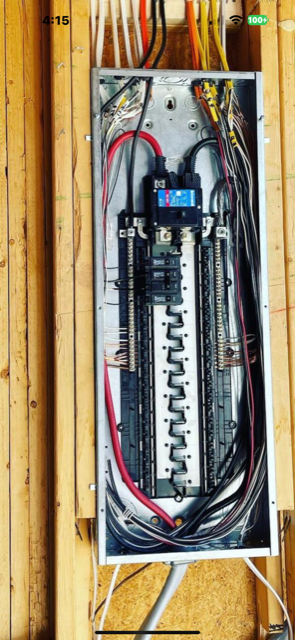 Open electrical breaker panel with wires and circuit breakers mounted on a wooden wall.